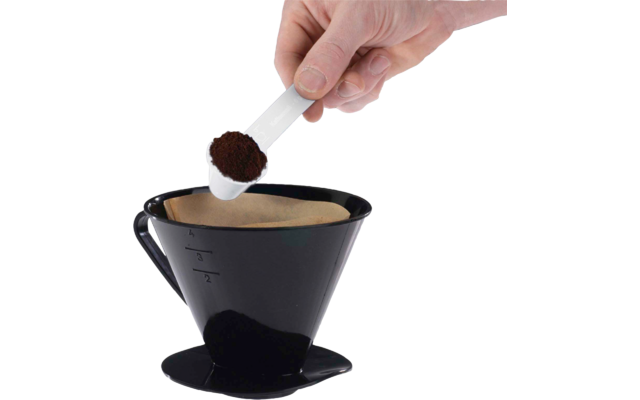 Main tenant une cuillère doseuse blanche de café moulu au-dessus d'un porte-filtre conique noir avec filtre en papier sur fond blanc