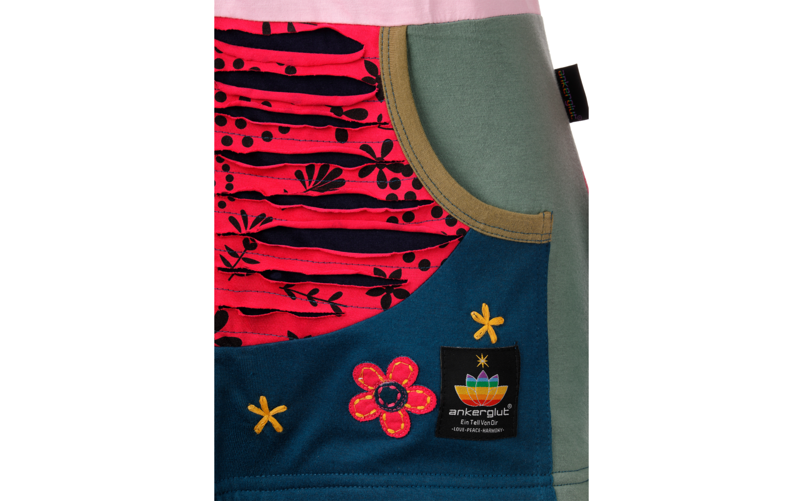 Gros plan sur un tissu coloré avec poche ronde : zone à motif rose et noir, côté vert, appliqués floraux cousus et étiquette noire avec logo multicolore