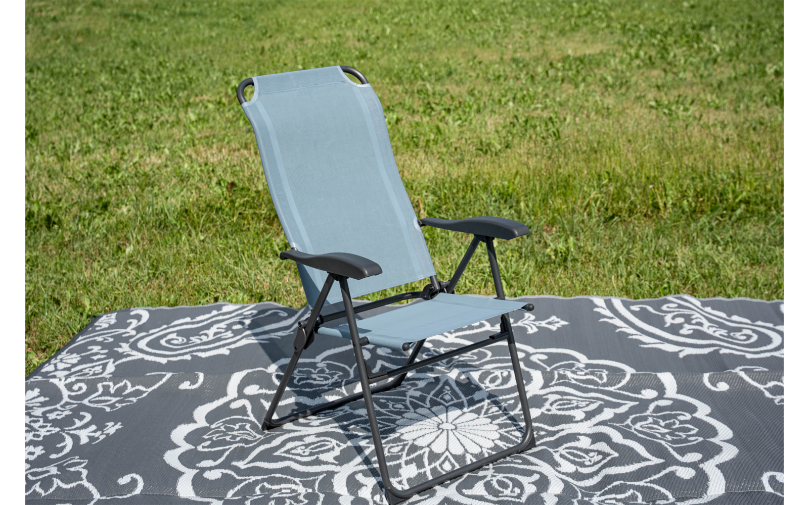 Sedia da giardino pieghevole azzurro chiaro con braccioli neri su una coperta grigia con motivo bianco sull'erba
