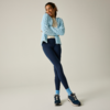 Persona de pie con las piernas cruzadas, brazos cruzados sobre el pecho, viste una chaqueta de forro polar azul claro, una camiseta blanca, mallas azul oscuro, calcetines azul claro y zapatillas deportivas azul oscuro sobre un fondo liso y neutro
