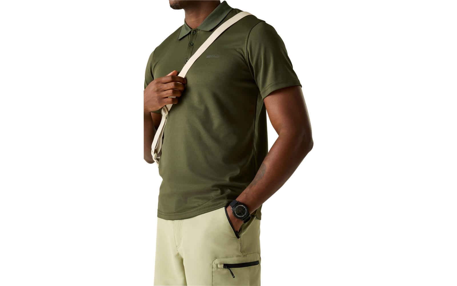 Person trägt olivgrünes Poloshirt und helle Cargohose, hat eine Umhängetasche über der Schulter, hält den Riemen mit der linken Hand, trägt eine Armbanduhr, steht vor hellem einfarbigem Hintergrund und blickt nach links