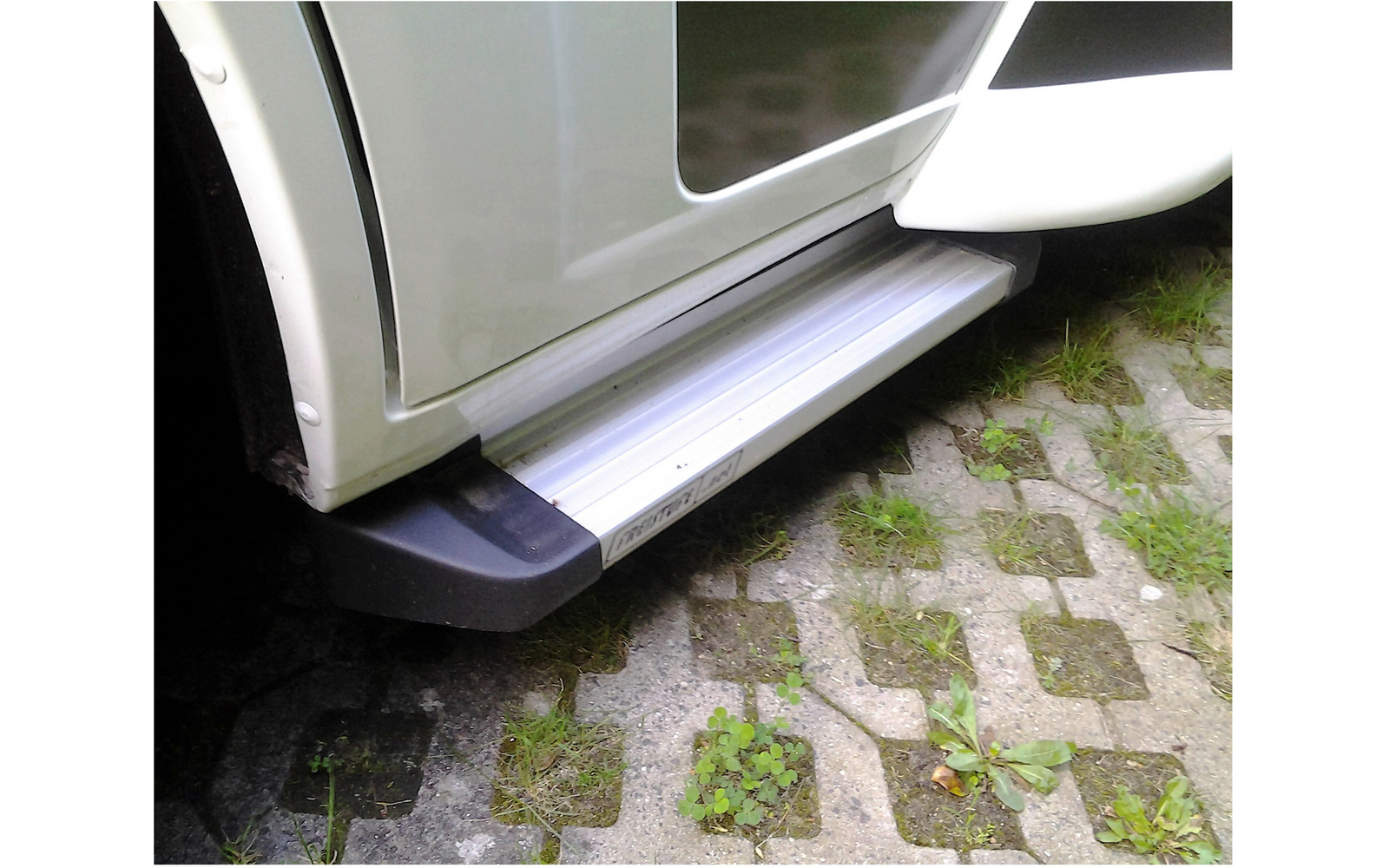 Marchepied replié sur un véhicule blanc garé sur un sol pavé avec de l'herbe