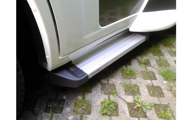 Eingeklapptes Trittbrett an weißem Fahrzeug, geparkt auf gepflastertem Untergrund mit Gras