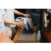Hands placing several plates in a dish rack on a drying mat on a countertop; a bottle of dish soap visible
