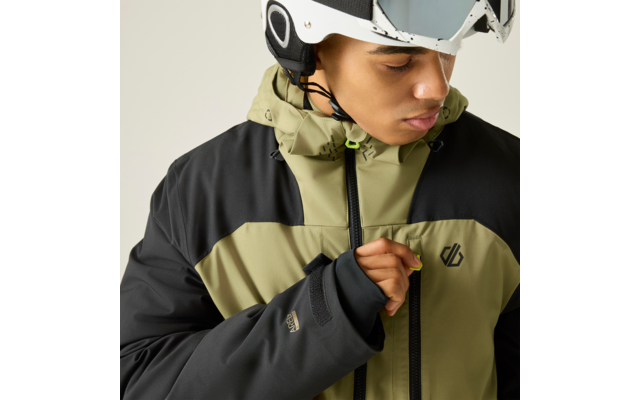 Person mit weißem Helm und hochgeschobener Skibrille trägt olivgrün-schwarze Jacke und zieht an einem neongrünen Reißverschluss-Anhänger