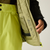 Hand hält eine geöffnete hellgrüne Jacke, Innenseite mit Pflegezeichen und Reißverschlussfach; hellgrüne Hose und schwarzer Jackenärmel sichtbar