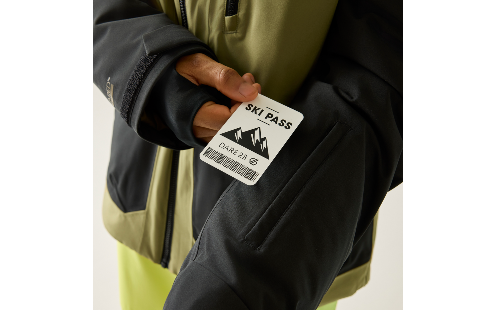 Hand hält eine Karte mit der Aufschrift "SKI PASS", Bergsymbol und Barcode vor einer schwarzen und olivgrünen Jacke