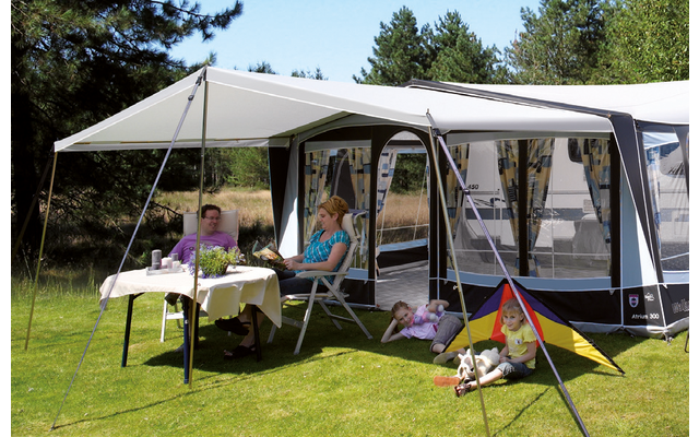 Personen sitzen an einem Tisch unter einem Sonnenschutz neben einem Wohnwagen im Freien