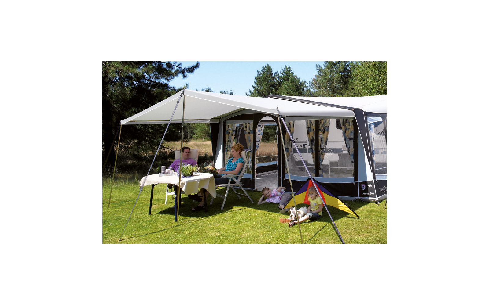 Personen sitzen an einem Tisch unter einem Sonnenschutz neben einem Wohnwagen im Freien