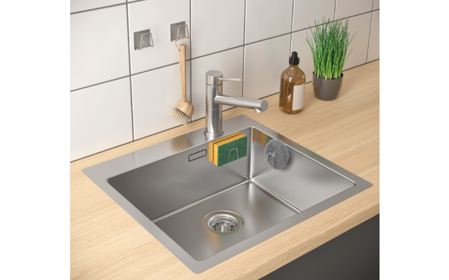 Küchenspüle aus Edelstahl mit Wasserhahn, Seifenspender und grünem Kraut auf der Arbeitsplatte