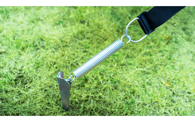 T-vormige metalen paal met bevestigde metalen spiraalveer, via een metalen ring verbonden met een zwarte band op groen gras