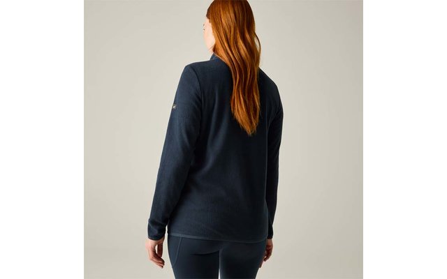 Vista trasera de una persona con cabello largo y rojo, viste una camiseta de manga larga azul marino y leggings, de pie sobre un fondo neutro claro