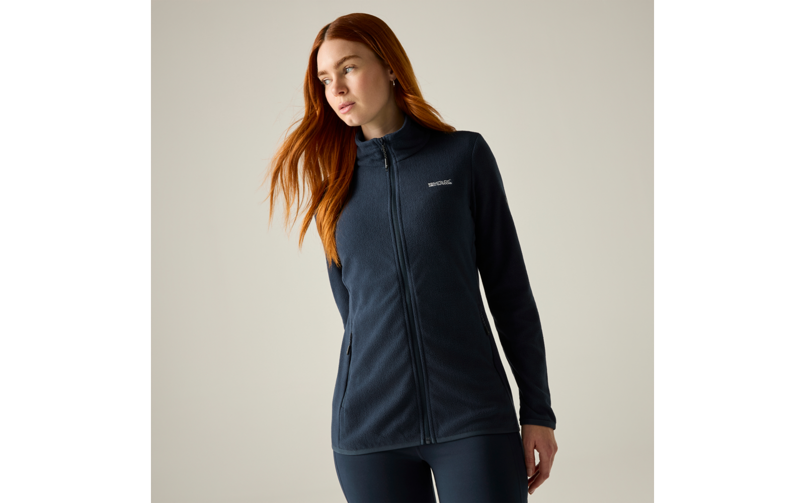 Persona con capelli lunghi rossi che indossa una giacca in pile blu scuro con cerniera e piccolo logo sul petto, su sfondo neutro
