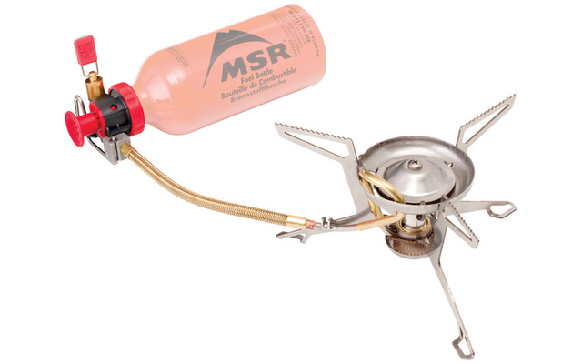 Metall-Tragkocher mit ausgeklappten Stützfüßen, per Schlauch mit oranger MSR-Treibstoffflasche verbunden