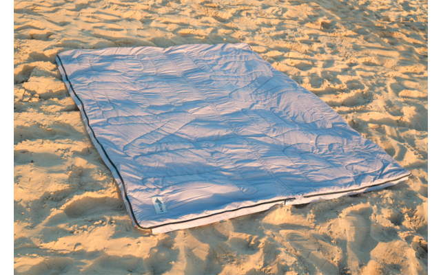 Sac de couchage bleu clair posé à plat sur le sable