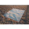 Couverture rectangulaire bleu clair posée sur du sable, ombres de feuilles de palmier sur la couverture