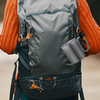 Rear view of a person in an orange knit sweater with a dark green backpack and a gray mug hanging from it