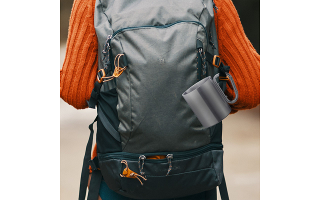 Rear view of a person in an orange knit sweater with a dark green backpack and a gray mug hanging from it