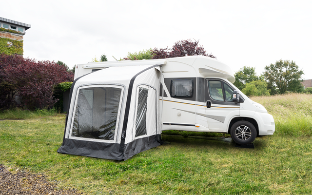 Weißes Wohnmobil mit angebautem Vorzelt auf einer grünen Wiese