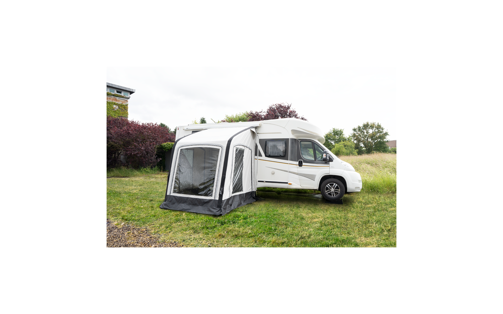 Weißes Wohnmobil mit angebautem Vorzelt auf einer grünen Wiese