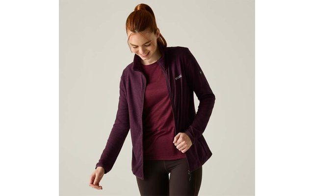 Donna con capelli rossi raccolti in una coda, guarda verso il basso e sorride, indossa una giacca con zip viola scuro aperta sopra una maglietta bordeaux e leggings neri su sfondo chiaro