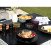 Black plates with various dishes on a wooden table outdoors
