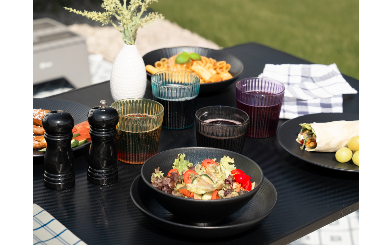 Black plates with various dishes on a wooden table outdoors