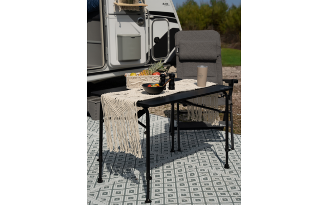 Stuhl und Tisch mit Decke und Flasche vor einem Wohnwagen im Freien