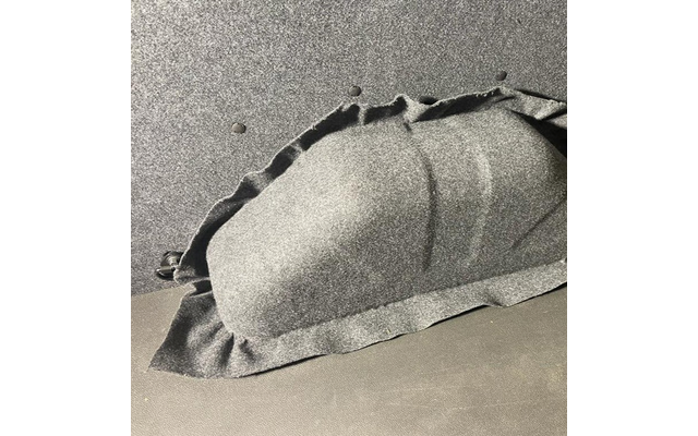 Gewelfde vorm onder zwart, grof getextureerd stof op een donkere ondergrond; stof met plooien en een zichtbare rand, twee kleine ronde openingen in het oppervlak erboven