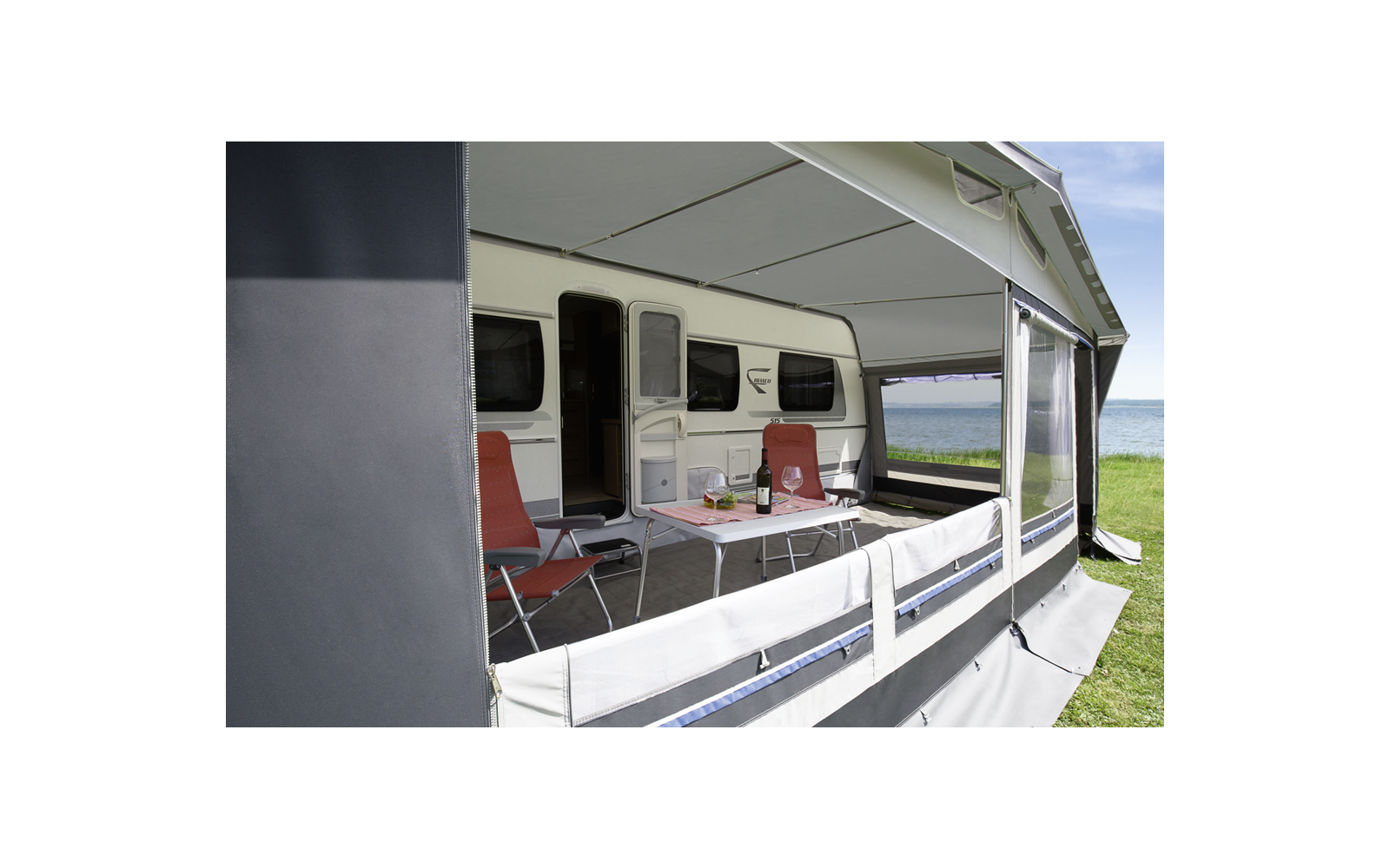 Weiße Markise über einer Terrasse mit Stühlen vor einem Wohnwagen