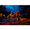 Vijf personen bij een kampeertafel in de schemering, proostend met drankjes; op de tafel een draagbare stroomvoorziening met kabels, een luidspreker, borden met hapjes en een smartphone; op de achtergrond een camper, bomen en een donkere lucht