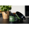 Tasse émaillée verte avec inscription blanche 'camp life' à côté d'un bol émaillé vert incliné; en arrière-plan un panier tressé avec une plante sur une table noire