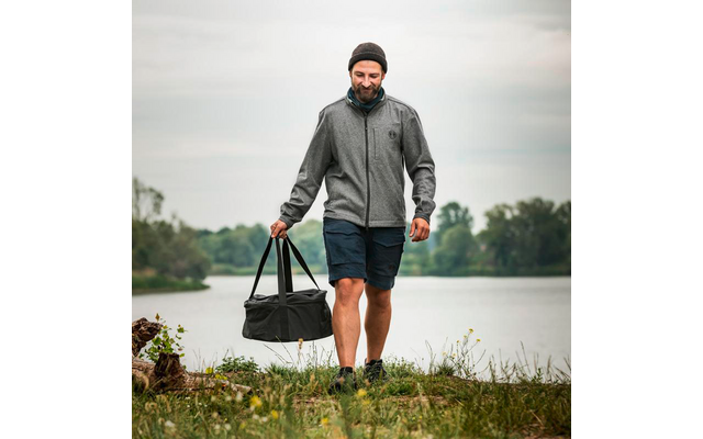 Mann mit Mütze trägt Sporttasche und geht am Flussufer