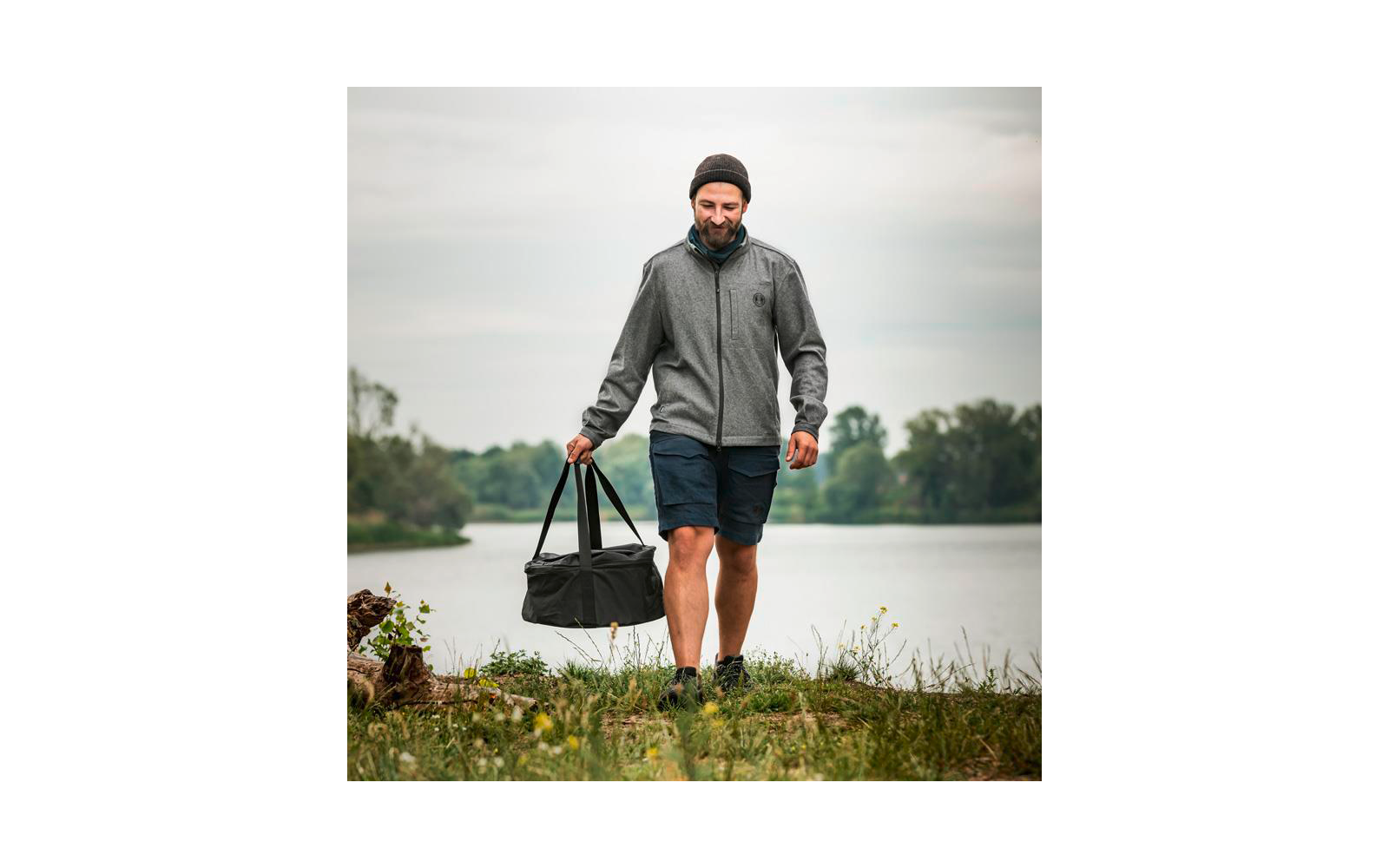 Mann mit Mütze trägt Sporttasche und geht am Flussufer