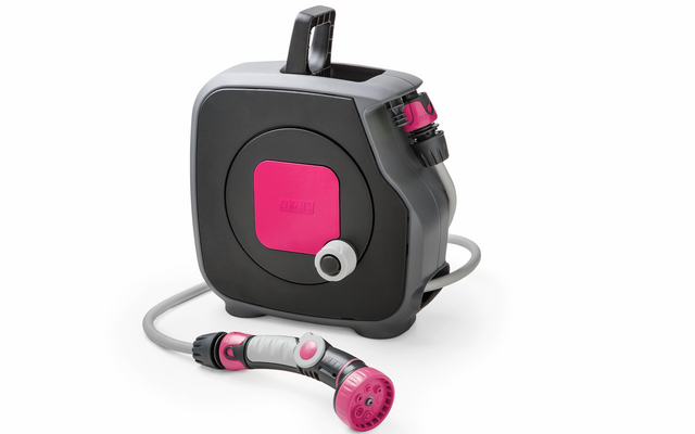 Viereckiges schwarzes Kunststoffgehäuse mit Tragegriff und pinker Mitte; grauer aufgerollter Schlauch mit rosa-grauer Sprühdüse liegt davor