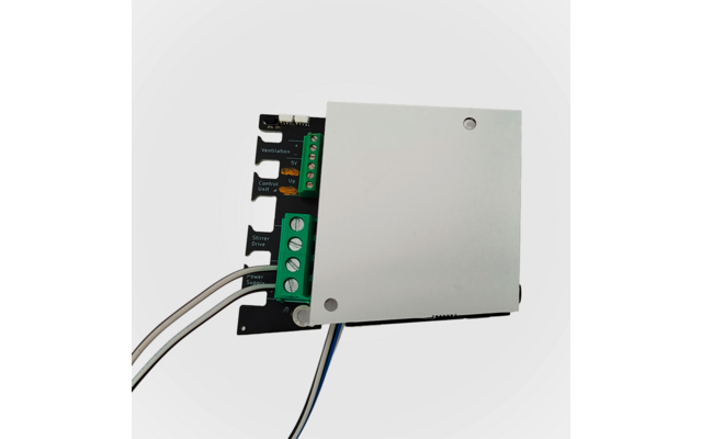 Leiterplatte mit silberner Abdeckung, grünem Schraubklemmenblock, mehrfarbigen Anschlussdrähten und zwei sichtbaren Befestigungslöchern vor weißem Hintergrund