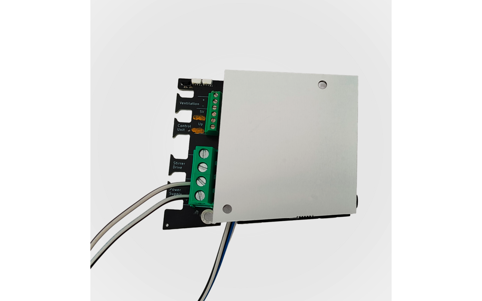 Leiterplatte mit silberner Abdeckung, grünem Schraubklemmenblock, mehrfarbigen Anschlussdrähten und zwei sichtbaren Befestigungslöchern vor weißem Hintergrund