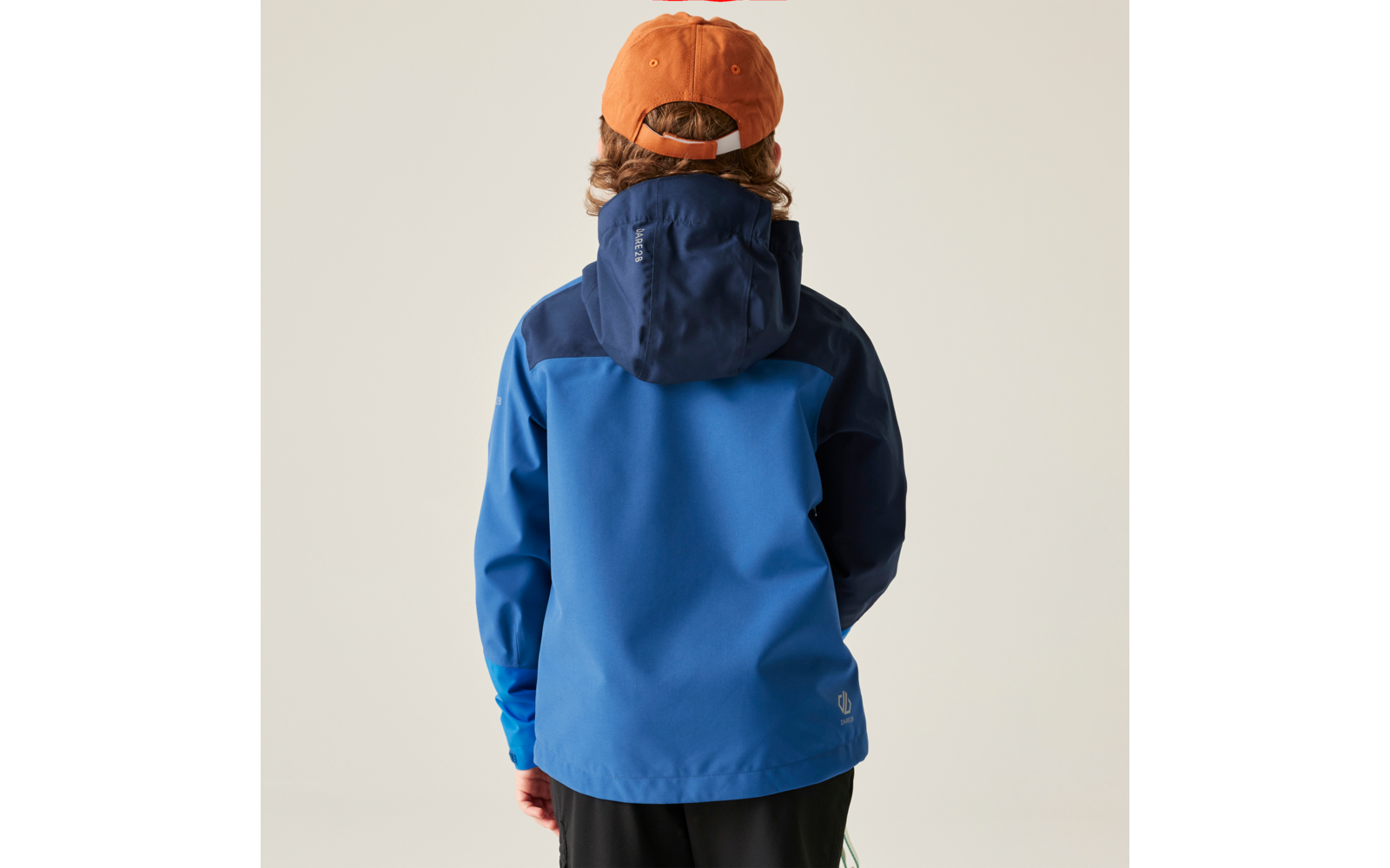 Rückansicht einer Person mit orangefarbener Baseballkappe, sichtbaren gewellten Haaren, zweifarbiger blauer Regenjacke und schwarzer Hose