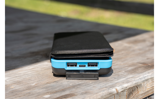 Blau-schwarzes Powerbank mit zwei USB-A-Anschlüssen, schwarzes Smartphone darauf, auf Holztisch