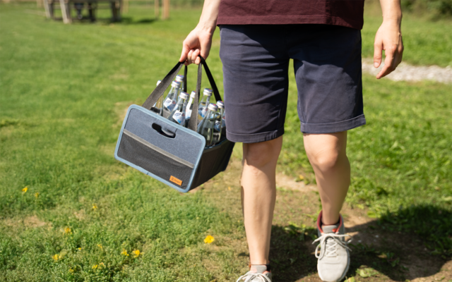 Person trägt einen kleinen Lautsprecher in der Hand, Spazierweg im Grünen