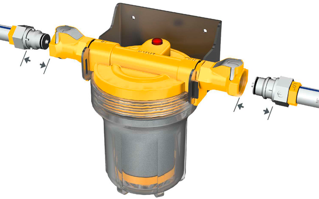 Boîtier jaune avec cuve cylindrique transparente en dessous, bouton rouge sur le dessus, support métallique en arrière-plan, raccords de tuyau à gauche et à droite avec attaches rapides et marquages de flèches noirs
