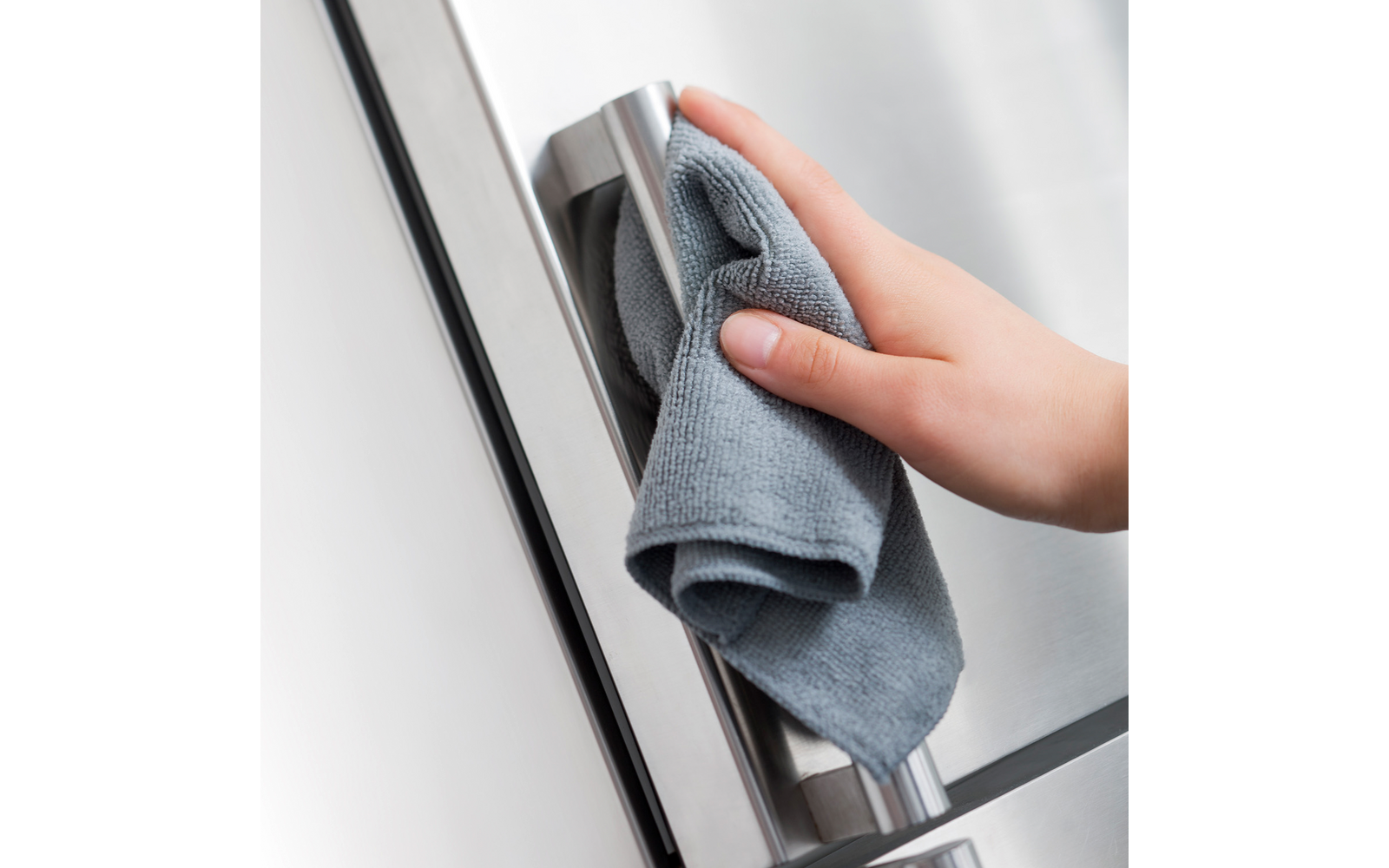 Hand hält graues Mikrofasertuch an einem Edelstahlgriff eines Kühlschranks