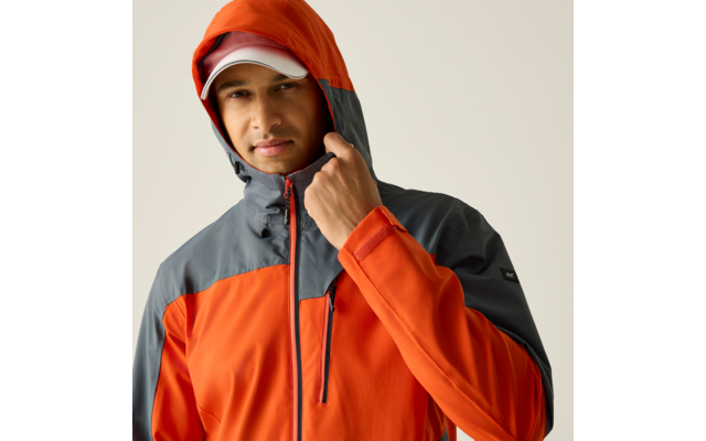 Person in orange-grauer Kapuzenjacke und weißer Kappe hält den Kapuzenrand vor hellem einfarbigem Hintergrund