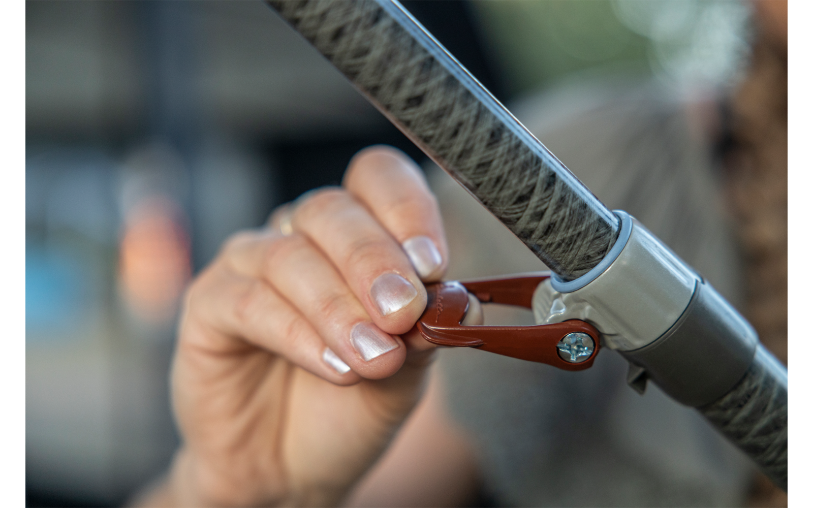 Hand mit französischer Maniküre fasst einen kleinen roten Hebel, der an einem grauen Rohr mit Metallklemme befestigt ist; unscharfer Hintergrund