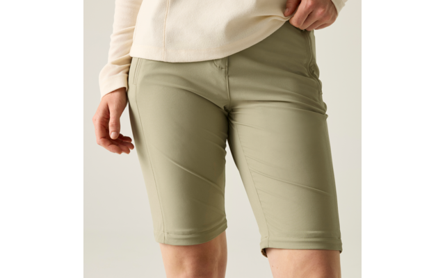 Unterkörper einer Person in hellgrünen knielangen Shorts und hellbeigem Oberteil, Hände seitlich sichtbar