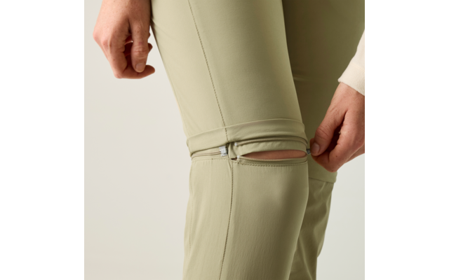 Nahaufnahme von hellgrünen Hosenbeinen mit einer Reißverschlussöffnung am Knie; Hände berühren den Reißverschluss