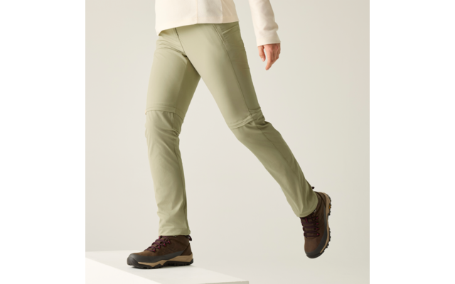 Beinpartie einer Person, die von einem weißen Podest steigt, hellgrüne Hose, cremefarbener Ärmel sichtbar, braune Schnürschuhe