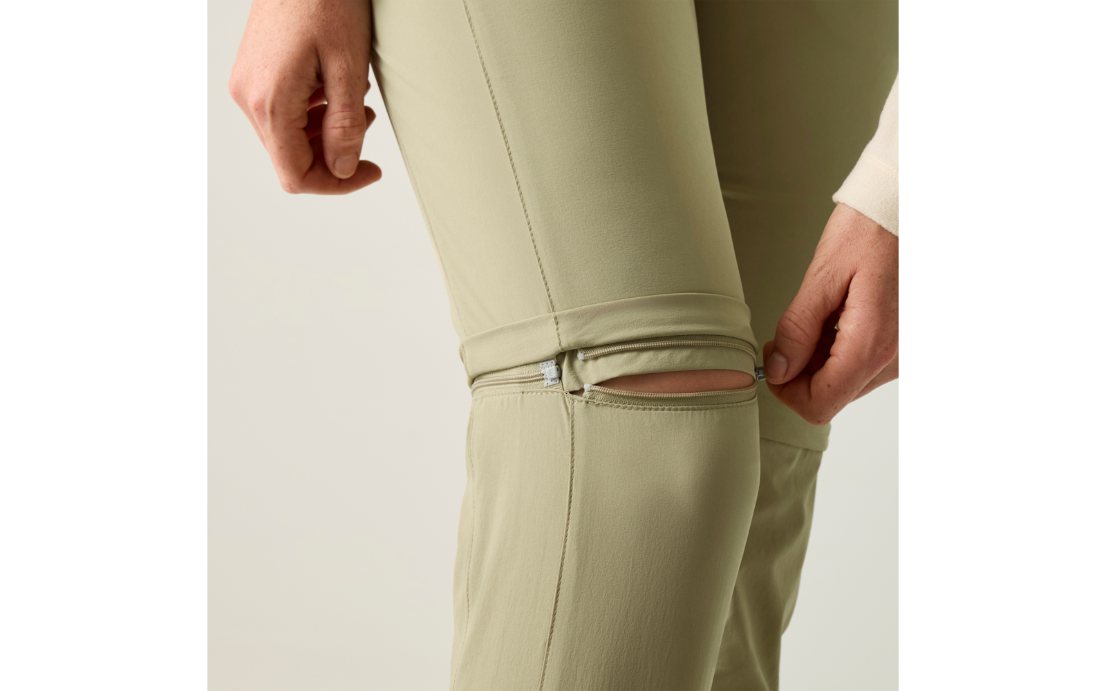 Nahaufnahme von hellgrünen Hosenbeinen mit einer Reißverschlussöffnung am Knie; Hände berühren den Reißverschluss