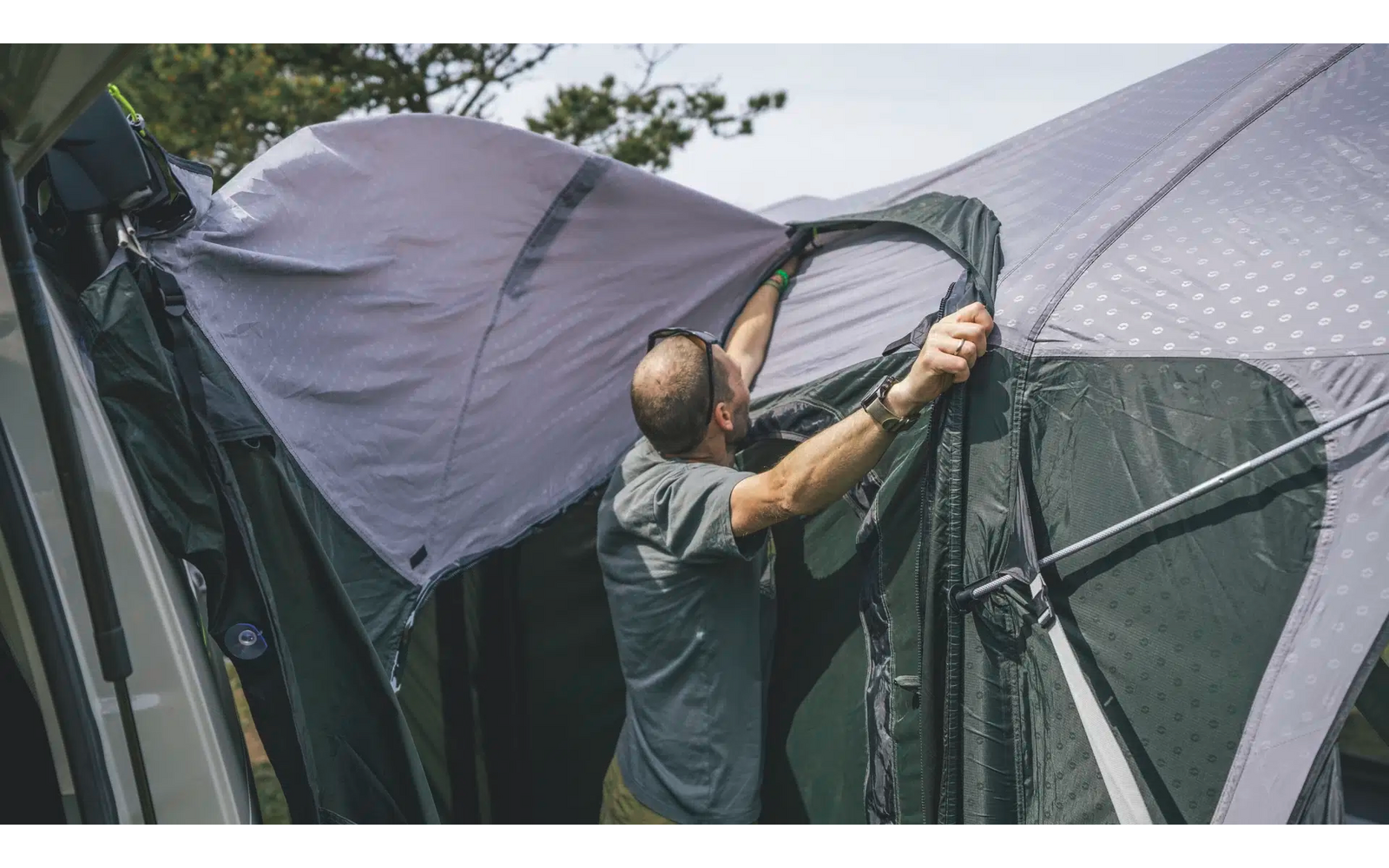 Eine Person befestigt ein graues Zelt an einem Auto