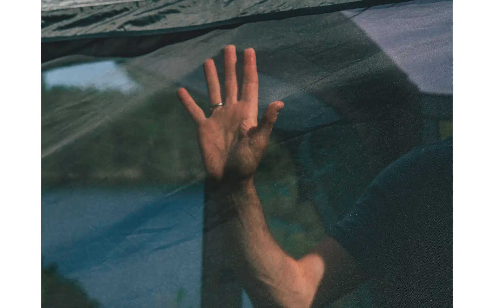 Eine Hand berührt eine Fensterscheibe von innen